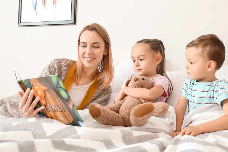 Nanny helping children adapt to a new environment by reading a bed-time story